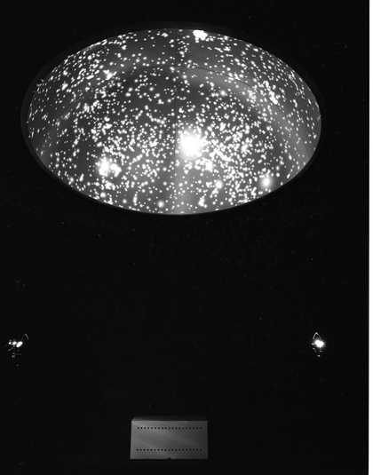 A dark room with a concave disc on its ceiling that features hundreds of tiny lights.