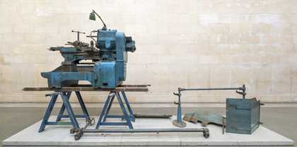 A piece of heavy machinery on a trestle bench on a plinth in a gallery
